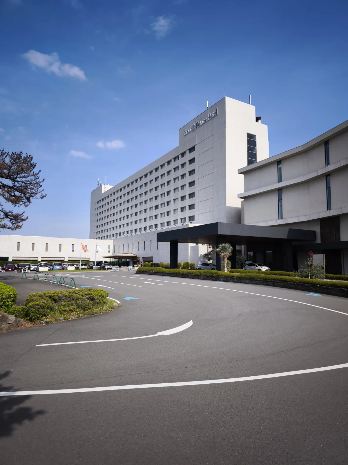 青空の下の大磯プリンスホテルの外観。車寄せとエントランス、手前に広い駐車場