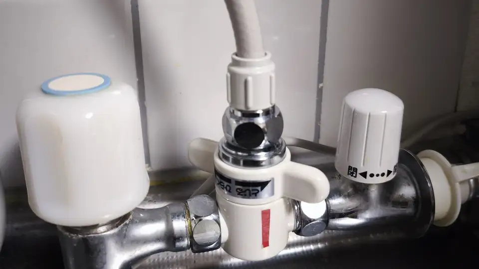 キッチンの蛇口まわり。分岐水栓に2分岐コックが付き、そこから整水器への白いホースが伸びている